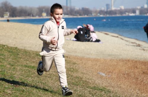 Young boy in a tracksuit runs energetically by the waterfront, embodying the joy of a sunny day outdoors.